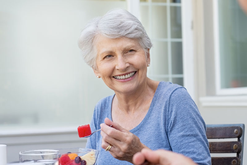 older person eating fruit with new denture