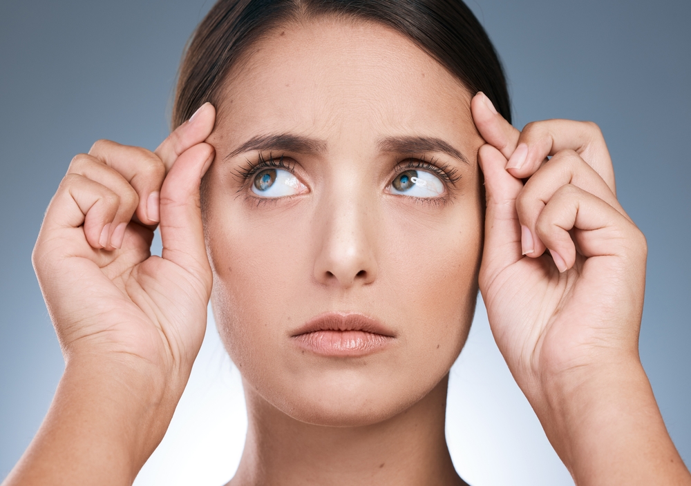 A woman looks up, pulling at her temples, possibly concerned about wrinkles, finding solutions at Riverside Family Dental